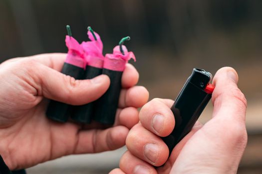 Setting Fire to the Several Firecrackers. Man in Black Jacket Lighting Up Three Petards at the Same Time. Firing Up the Pyrotechnic with Black Gas Lighter Outdoors