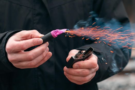 The Firecracker in a Hand. Man Holding a Burning Petard in His Hand. A Human with a Pyrotechnics that Burns with Sparks and Smoke Outdoors