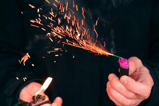 The Firecracker in a Hand. Man Holding a Burning Petard in His Hand. A Human with a Pyrotechnics that Burns with Sparks and Smoke Outdoors