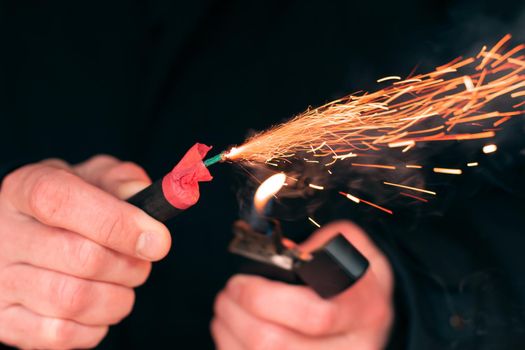 The Firecracker in a Hand. Man Holding a Burning Petard in His Hand. A Human with a Pyrotechnics that Burns with Sparks and Smoke Outdoors