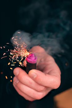 The Firecracker in a Hand. Man Holding a Burning Petard in His Hand. A Human with a Pyrotechnics that Burns with Sparks and Smoke Outdoors