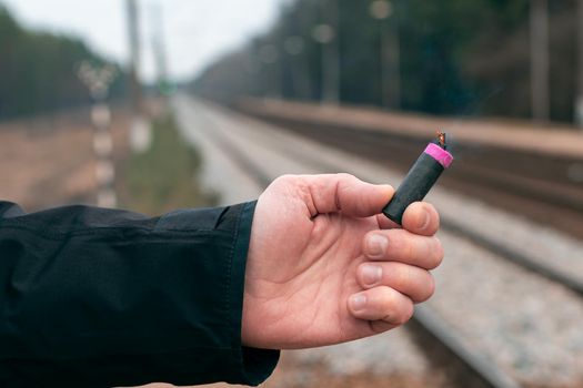 The Firecracker in a Hand. Man Holding a Burning Petard in His Hand. A Human with a Pyrotechnics that Burns with Sparks and Smoke Outdoors