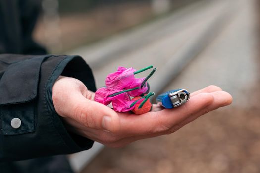 The Firecrackers in a Hand. Man Holding Five Black Petards with a Blue Gas Lighter on His Palm. A Human with a Pyrotechnics Outdoors