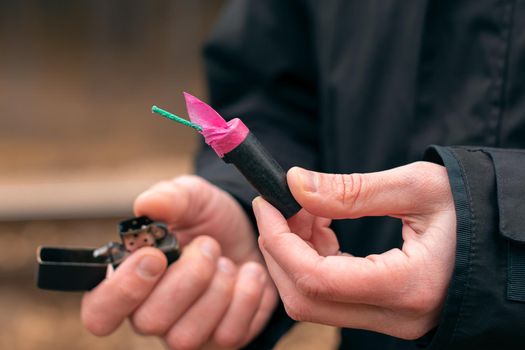 Setting Fire to the Firecracker. Man in Black Clothes Lighting Up the Petard. Firing Up the Pyrotechnics with a Black Gasoline Lighter Outdoors