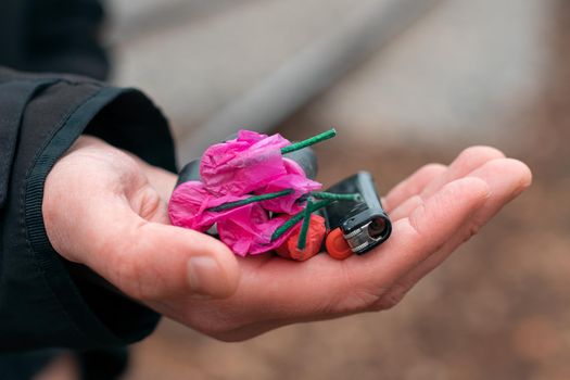 The Firecrackers in a Hand. Man Holding Five Black Petards with a Gas Lighter on His Palm. A Human with a Pyrotechnics Outdoors