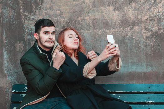 Cheerful Emotional Young Couple Sitting on the Bench and Making Selfie. Two Happy People Love Story on the Street