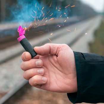 The Firecracker in a Hand. Man Holding a Burning Petard in His Hand. A Human with a Pyrotechnics that Burns with Sparks and Smoke Outdoors