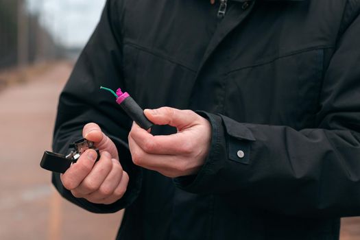 Setting Fire to the Firecracker. Man in Black Clothes Lighting Up the Petard. Firing Up the Pyrotechnics with a Black Gasoline Lighter Outdoors