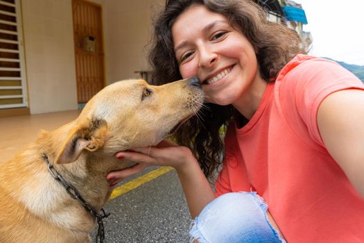 A beautiful brunette girl makes a selfie with her beloved dog. The dog is very happy and excited kisses the girl. Pets and their owners.