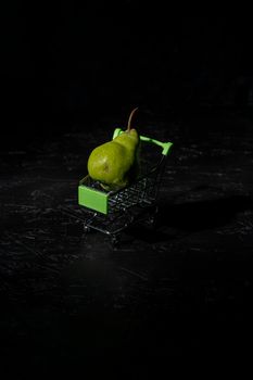 pear in the tiny supermarket cart on black. The concept of healthy eating