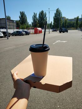 Fast food takeaway. Craft box with pizza and a glass of hot drink in hand. Snack on the go.