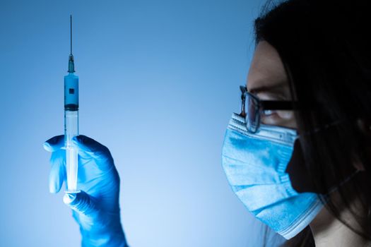 Young female doctor in a medical mask and gloves holds a syringe with a coronavirus vaccine and a vaccine chip inside. Conspiracy theory. Chipping people.