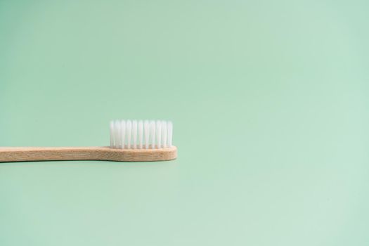 Environmentally friendly bamboo wood antibacterial toothbrush on light green background.