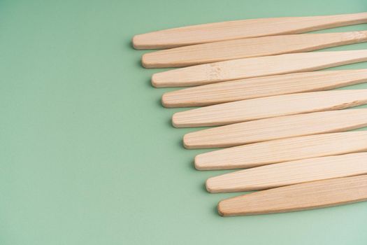 A set of Eco-friendly antibacterial toothbrushes made of bamboo wood on a light green background. Environmental care trends.