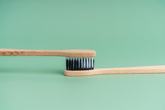 Two Eco-friendly antibacterial bamboo wood toothbrushes with white and black bristles on a light green background. Taking care of the environment is trending. Tolerance. Copy space.