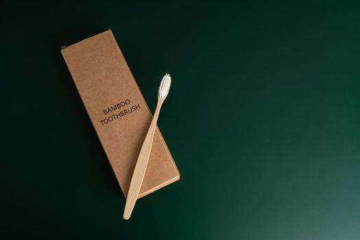 Eco-friendly antibacterial bamboo wood toothbrush on dark green background. Taking care of the environment in trend.