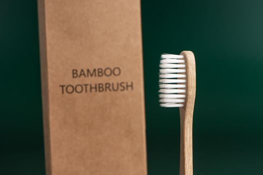 Eco-friendly antibacterial bamboo wood toothbrush on dark green background. Taking care of the environment in trend.