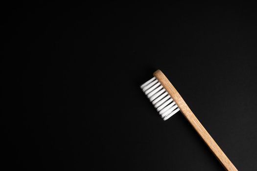 Eco-friendly antibacterial bamboo wood toothbrush with white bristles on a black background. Taking care of the environment is trending. Copy space.