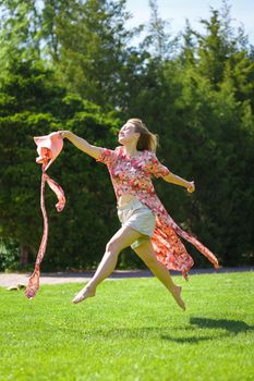 A charming girl in a light summer sundress and a pareo hat is walking in a green park. Enjoys warm sunny summer days.