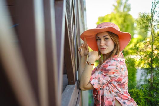 A charming girl in a light summer sundress and a pareo hat is walking in a green park. Enjoys warm sunny summer days.