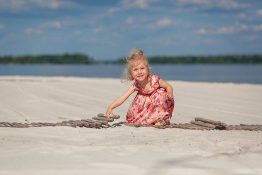 A little girl in a beautiful sarafna plays in the sand on the beach.