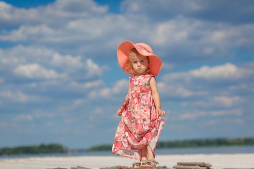 A little girl in a beautiful sarafna plays in the sand on the beach.