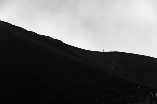 Minimalist image of small silhouette of men climbing on the edge of Etna volcano crater with a cloudy background