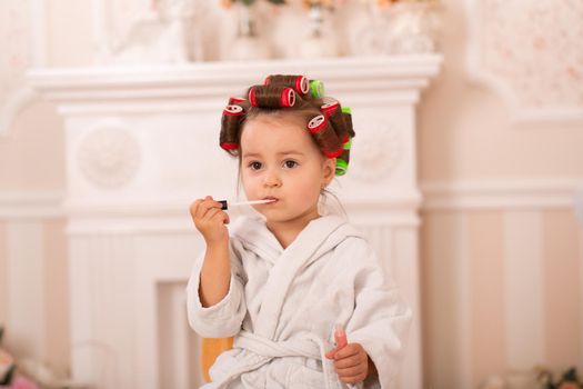 Adorable little girl with her mother in hair curlers apply makeup. Mom teaches daughter to use cosmetics. Beauty day. Girls are such girls.