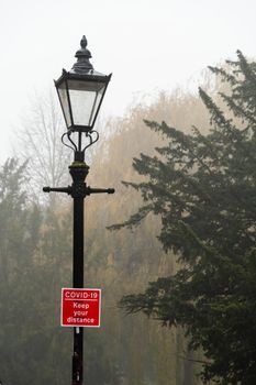Covid-19 keep apart red sign to encourage social distancing during 2020 coronavirus pandemic. Sign attached to a lamp and captured in a gloomy, foggy and rainy day Cambridge, UK