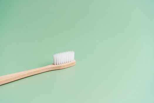Environmentally friendly bamboo wood antibacterial toothbrush on light green background.