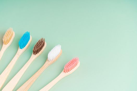 A set of Eco-friendly antibacterial toothbrushes made of bamboo wood on a light green background. Environmental care trends.