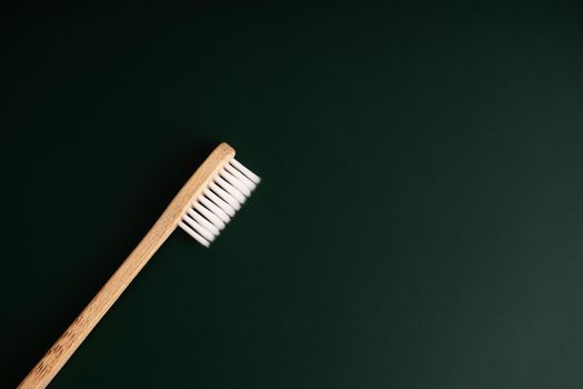 Eco friendly dental health antibacterial bamboo wood toothbrush on dark green background.