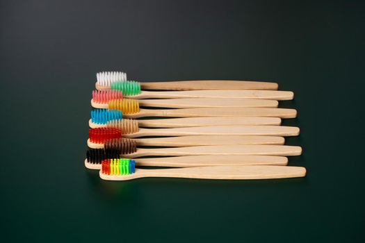 A set of Eco-friendly antibacterial toothbrushes made of bamboo wood on a dark green background. Environmental trends.