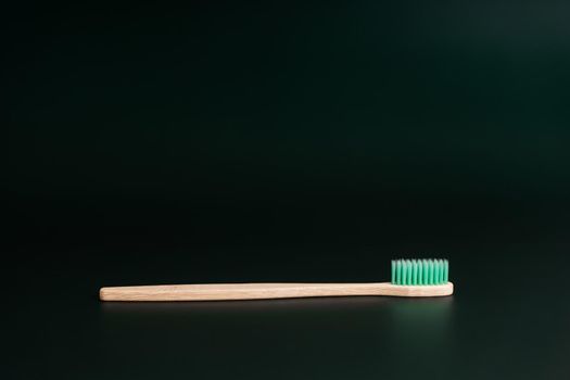 Eco-friendly antibacterial bamboo wood toothbrush on dark green background. Taking care of the environment in trend.