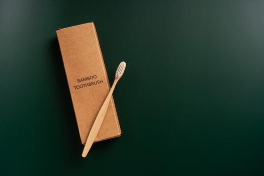 Eco-friendly antibacterial bamboo wood toothbrush on dark green background. Taking care of the environment in trend.