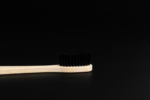 Eco friendly antibacterial bamboo wood toothbrush with black bristles on dark green background. Taking care of the environment in trend.