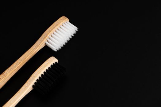 Two Eco-friendly antibacterial bamboo wood toothbrushes with white and black bristles on a black background. Taking care of the environment is trending. Tolerance. Copy space.