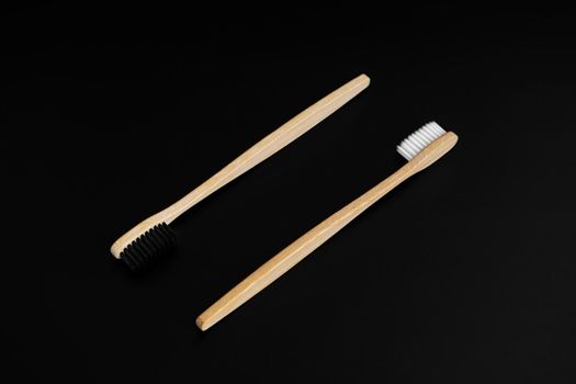 Two Eco-friendly antibacterial bamboo wood toothbrushes with white and black bristles on a black background. Taking care of the environment is trending. Tolerance. Copy space.