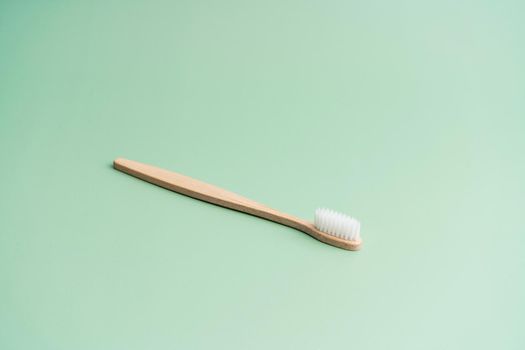 Environmentally friendly bamboo wood antibacterial toothbrush on light green background.