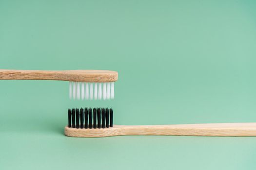 Two Eco-friendly antibacterial bamboo wood toothbrushes with white and black bristles on a light green background. Taking care of the environment is trending. Tolerance. Copy space.