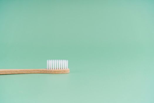 Environmentally friendly bamboo wood antibacterial toothbrush on light green background.