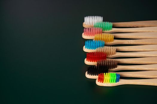 A set of Eco-friendly antibacterial toothbrushes made of bamboo wood on a dark green background. Environmental trends.