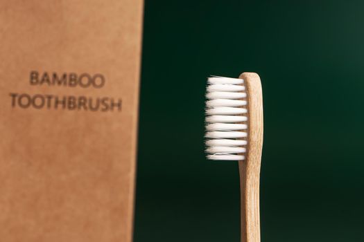 Eco-friendly antibacterial bamboo wood toothbrush on dark green background. Taking care of the environment in trend.