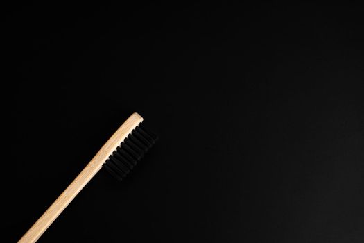 Eco friendly antibacterial bamboo wood toothbrush with black bristles on dark green background. Taking care of the environment in trend.