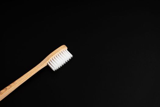 Eco-friendly antibacterial bamboo wood toothbrush with white bristles on a black background. Taking care of the environment is trending. Copy space.