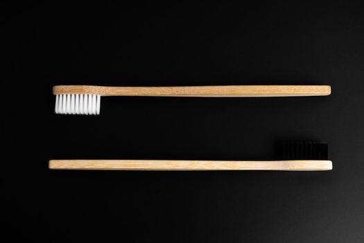 Two Eco-friendly antibacterial bamboo wood toothbrushes with white and black bristles on a black background. Taking care of the environment is trending. Tolerance. Copy space.