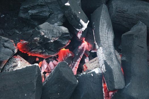 Fire on logs in fire pot with embers and burning coal. Bonfire with blazing red and orange fire flames. Fire background with woods and planks on fire at night view.