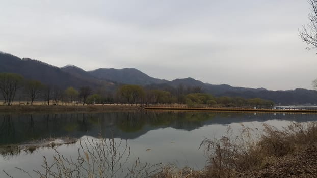 View of beautiful scene of river water and green trees on large hills on a sunny day with blue sky in background. A lovely landscape with breathtaking view over the horizon .