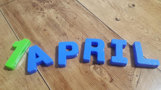 Plastic colored alphabets making words April are placed on a wooden floor. These plastic letters can be used for teaching kids.