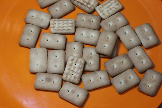 Close up top view of of biscuit cookies. Many rectangular biscuits with small pores in red plate